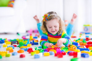 Little girl playing with toy blocks Cute funny preschooler little girl in a colorful shirt playing with construction toy blocks building a tower in a sunny kindergarten room